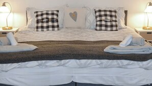 A neatly made bed with checkered pillows, a heart-shaped pillow, and two bedside lamps.