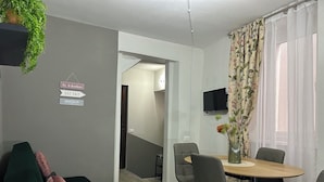 A modern living room with a green sofa, a dining table with chairs, a TV mounted on the wall, and a staircase leading to another room. - Timco apartment with lake view (Torno)
