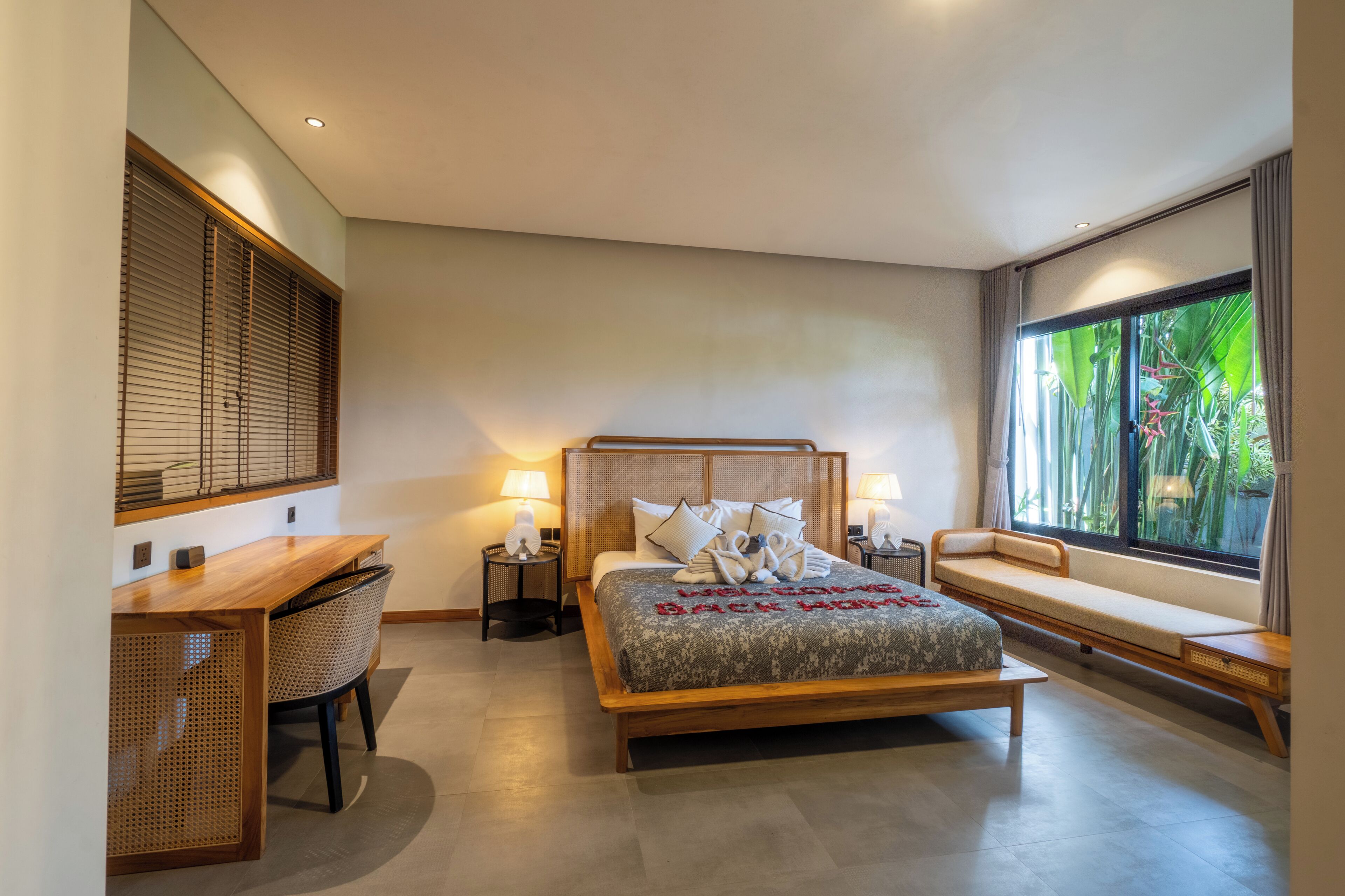A modern bedroom with a wooden bed, a desk, and a window with a view of greenery.