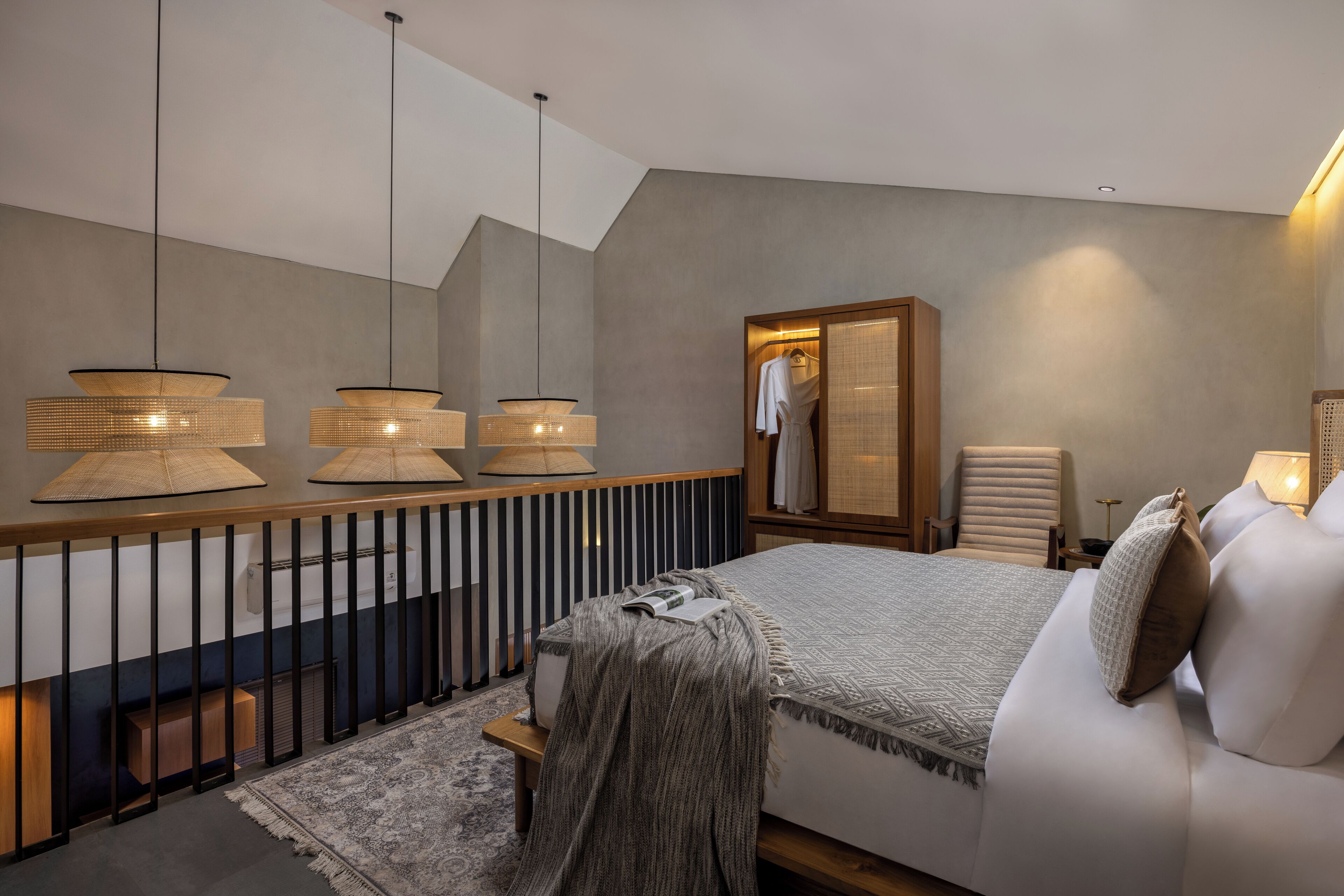 A modern bedroom with a large bed, bedside lamps, a wooden headboard, a mirror, and a seating area with a chair and a small table.