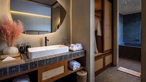 Une salle de bain moderne avec un grand miroir, un lavabo blanc et un meuble-lavabo en bois. On y trouve des serviettes et des articles de toilette sur le comptoir.