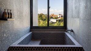 Une salle de bain moderne dotée d’une grande fenêtre, d’un carrelage à motifs hexagonaux et offrant une vue sur le quartier environnant.