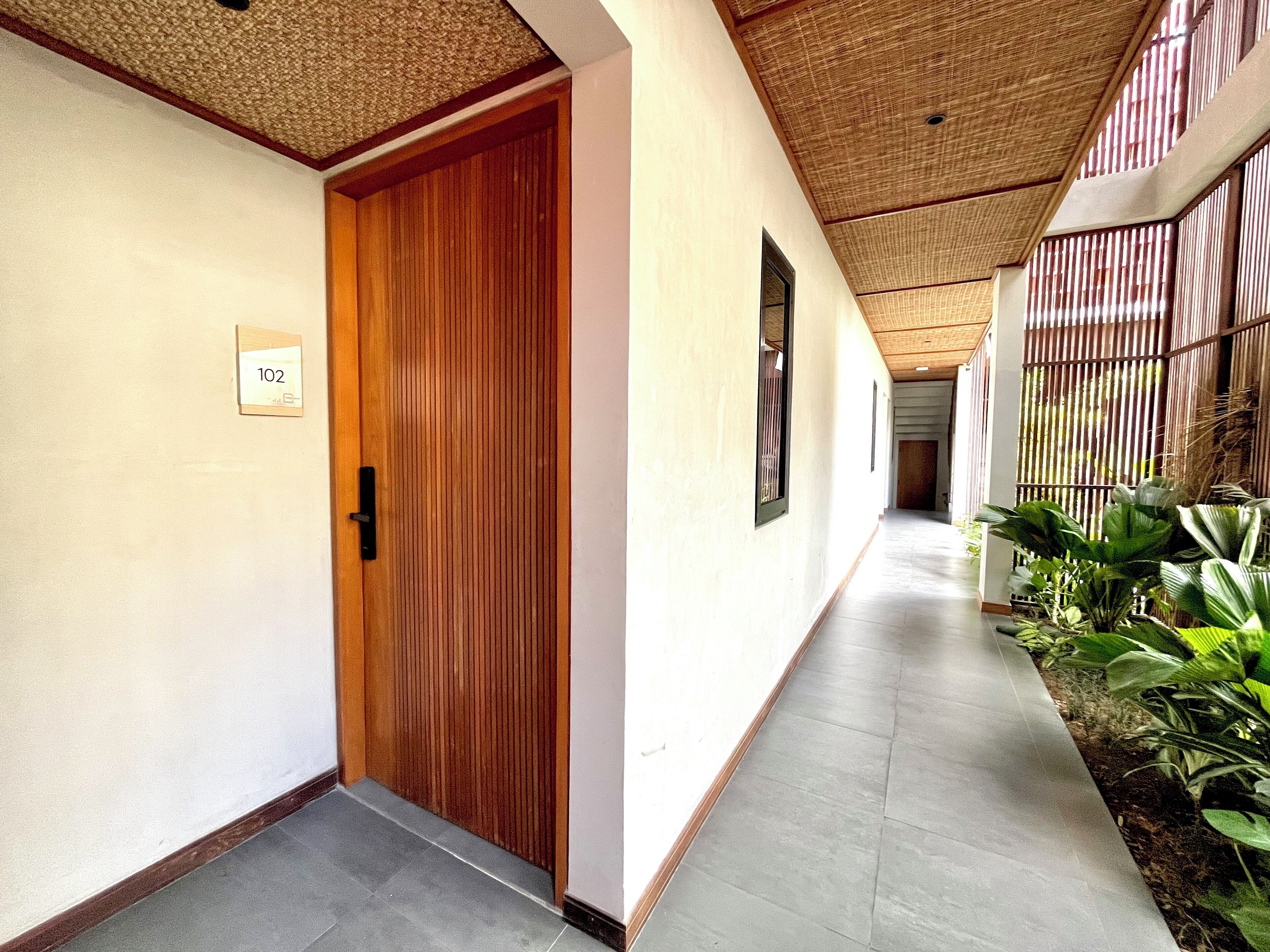A hallway with a wooden door labeled "102", a tiled floor, and a bamboo ceiling.