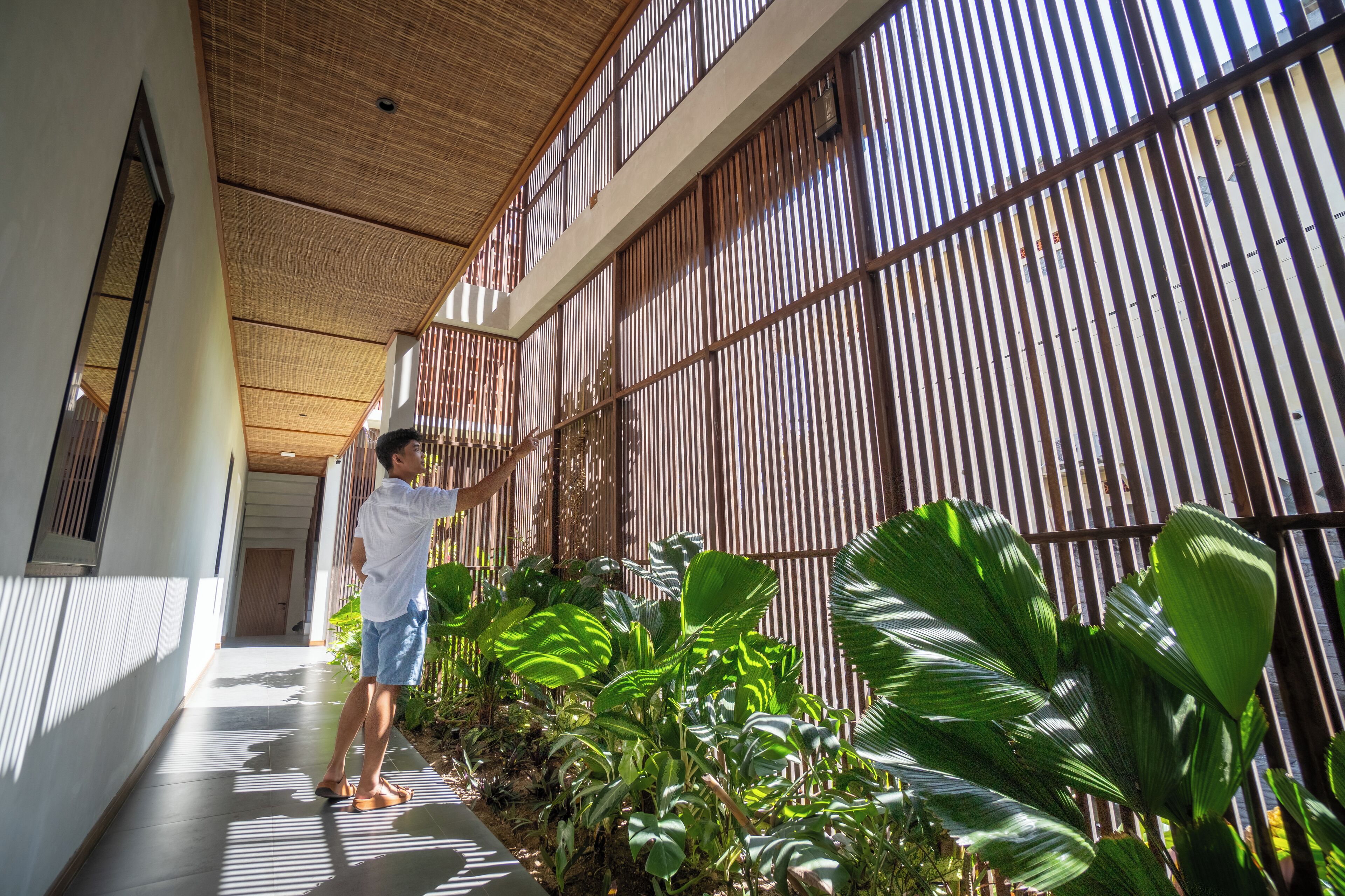 Un couloir avec un plafond en bambou, une personne debout et de nombreuses plantes vertes luxuriantes.