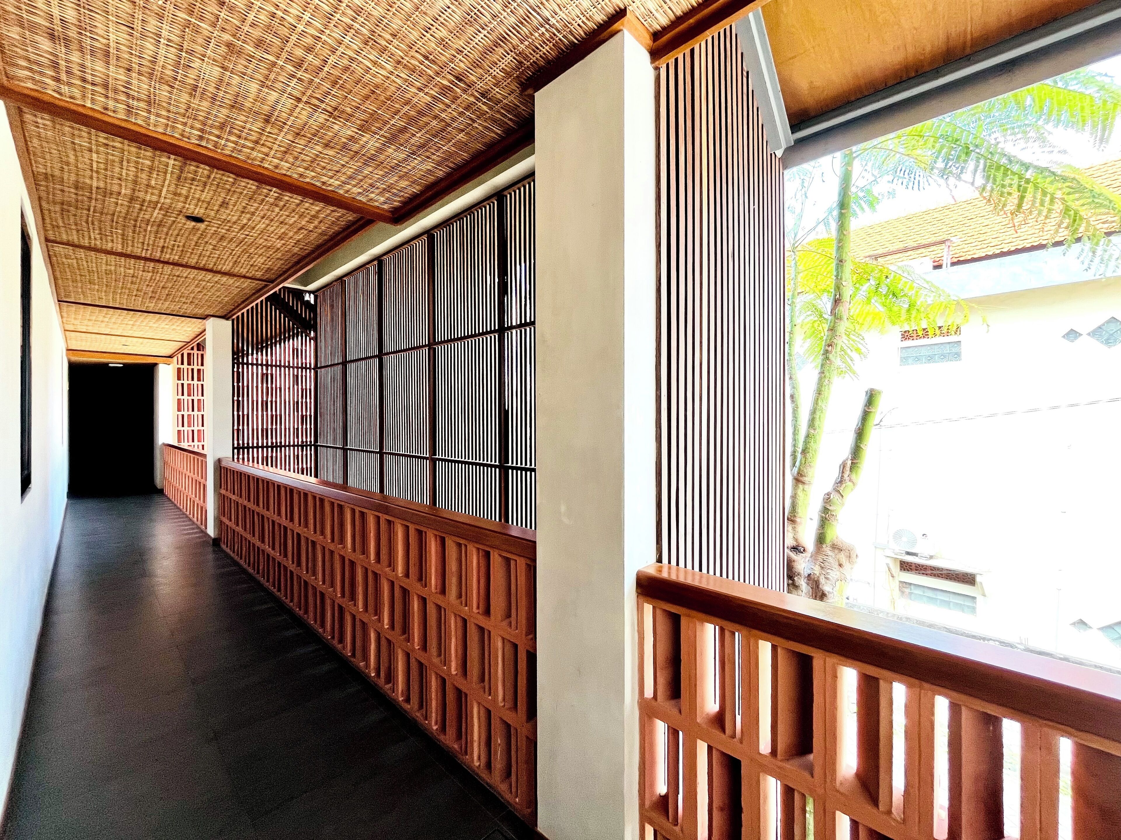A corridor with a bamboo ceiling, wooden railings, and a view of a residential area outside.