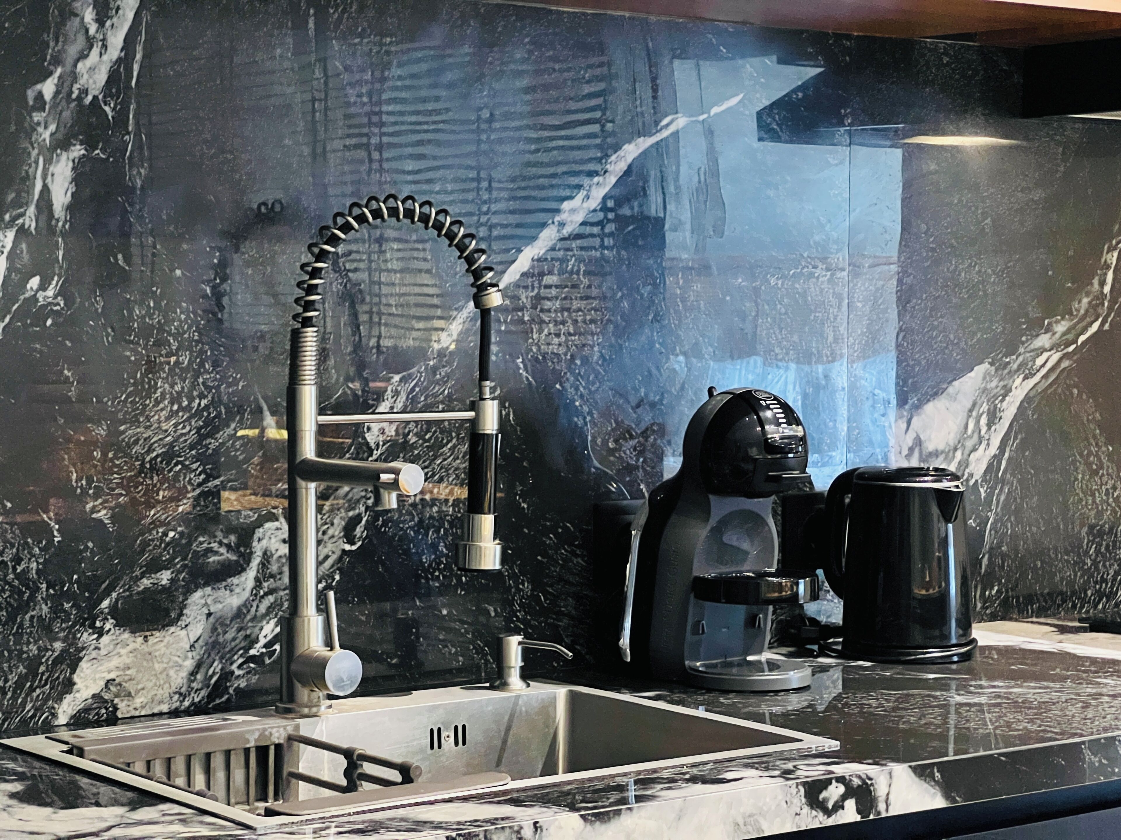 A kitchen with a modern faucet, a coffee maker, and a coffee pot on a marble countertop.