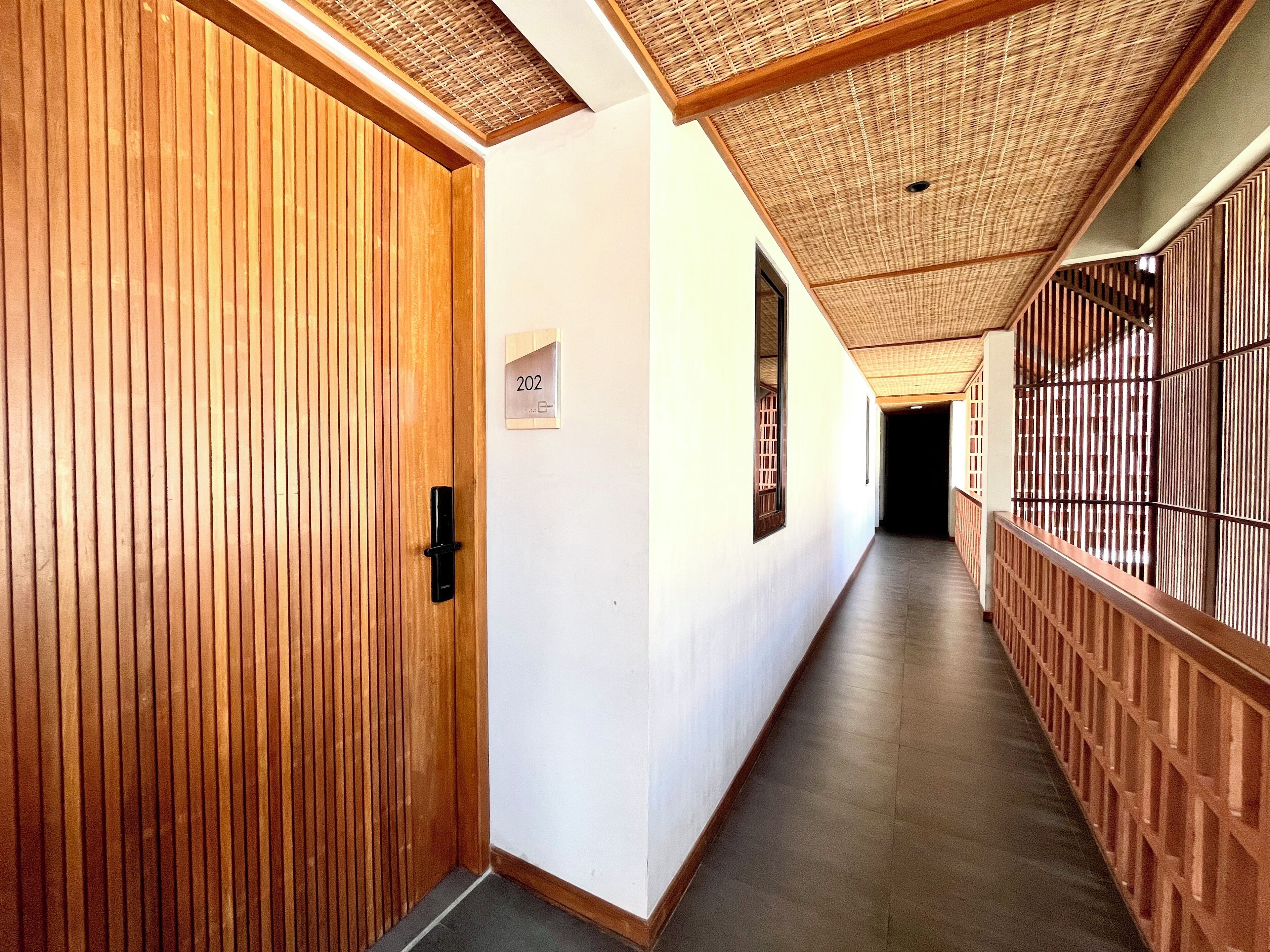 A corridor with wooden paneling, a sign with the number 202, and a ceiling with a woven pattern.