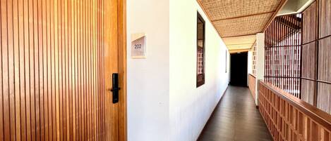 A corridor with wooden paneling, a sign with the number 202, and a ceiling with a woven pattern.