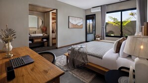 Une chambre moderne avec un lit, un bureau et un ordinateur portable. On y trouve une salle de bain avec un miroir et un lavabo. La chambre est dotée d’une grande fenêtre avec des rideaux.