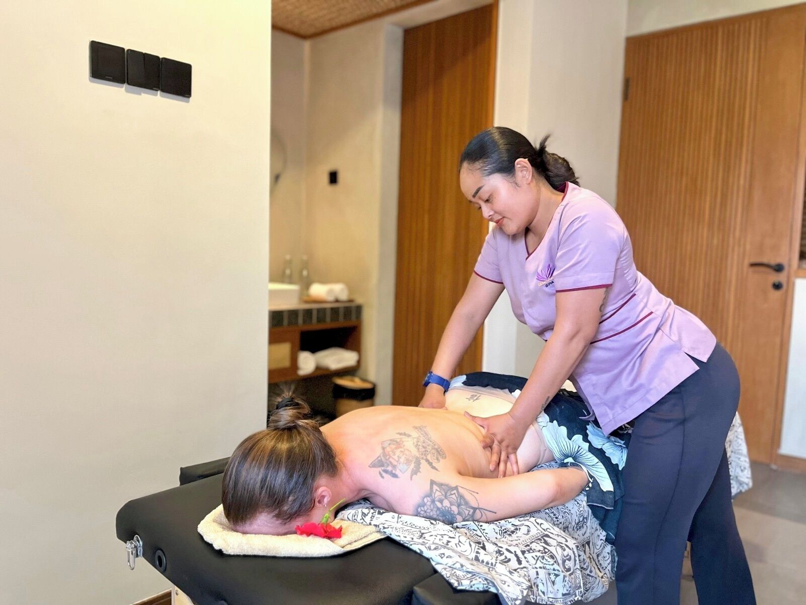 A massage therapy session in a room with a wooden door and a shelf with towels.