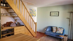 Ein gemütlicher Wohnbereich mit einer Holztreppe, einem blauen Sofa und einem Esstisch.