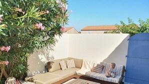 Ein gemütlicher Sitzbereich im Freien mit einer Couch, Kissen, einem kleinen Tisch und einem Sessel.