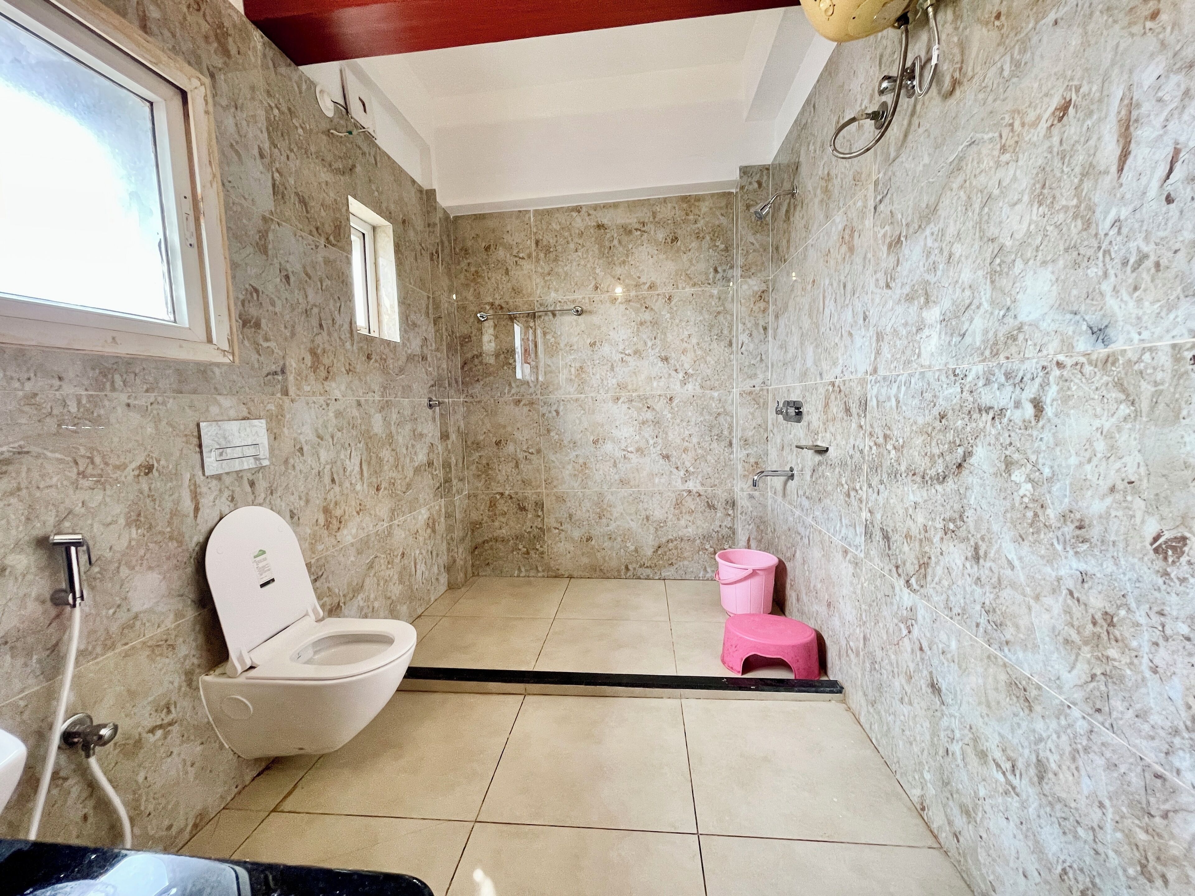 A bathroom with a shower, toilet, and a small pink stool.