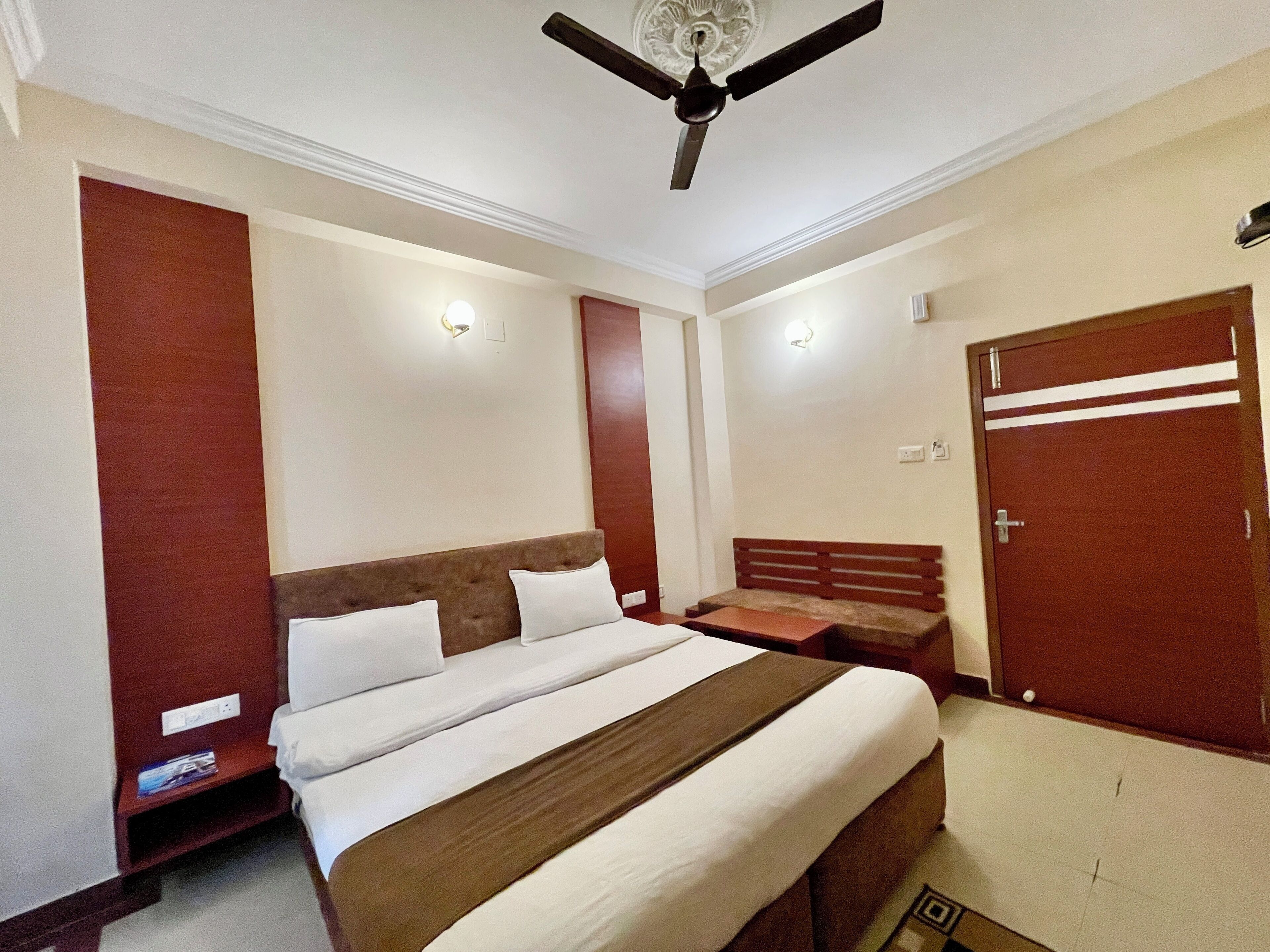 A hotel room with a large bed, a ceiling fan, a wardrobe, and a bedside table.