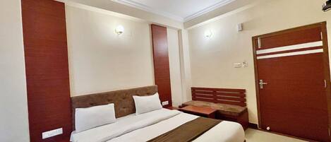 A hotel room with a large bed, a ceiling fan, a wardrobe, and a bedside table.