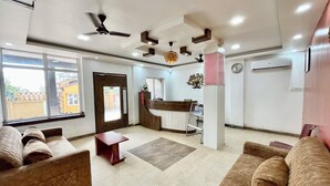 A hotel lobby with a reception desk, sofas, a coffee table, a clock, and an air conditioning unit. - Hotel Subham Beach Inn - near Sea Beach (Puri)