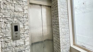 An elevator with a stone wall design, a control panel, and a window with a view of the outside. - Hotel Subham Beach Inn - near Sea Beach (Puri)