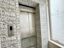 Un ascenseur dont les parois sont décorées de pierres, doté d’un panneau de commande et d’une fenêtre offrant une vue sur l’extérieur.