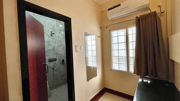 Un bagno con doccia, uno specchio, una finestra con tende e un condizionatore.