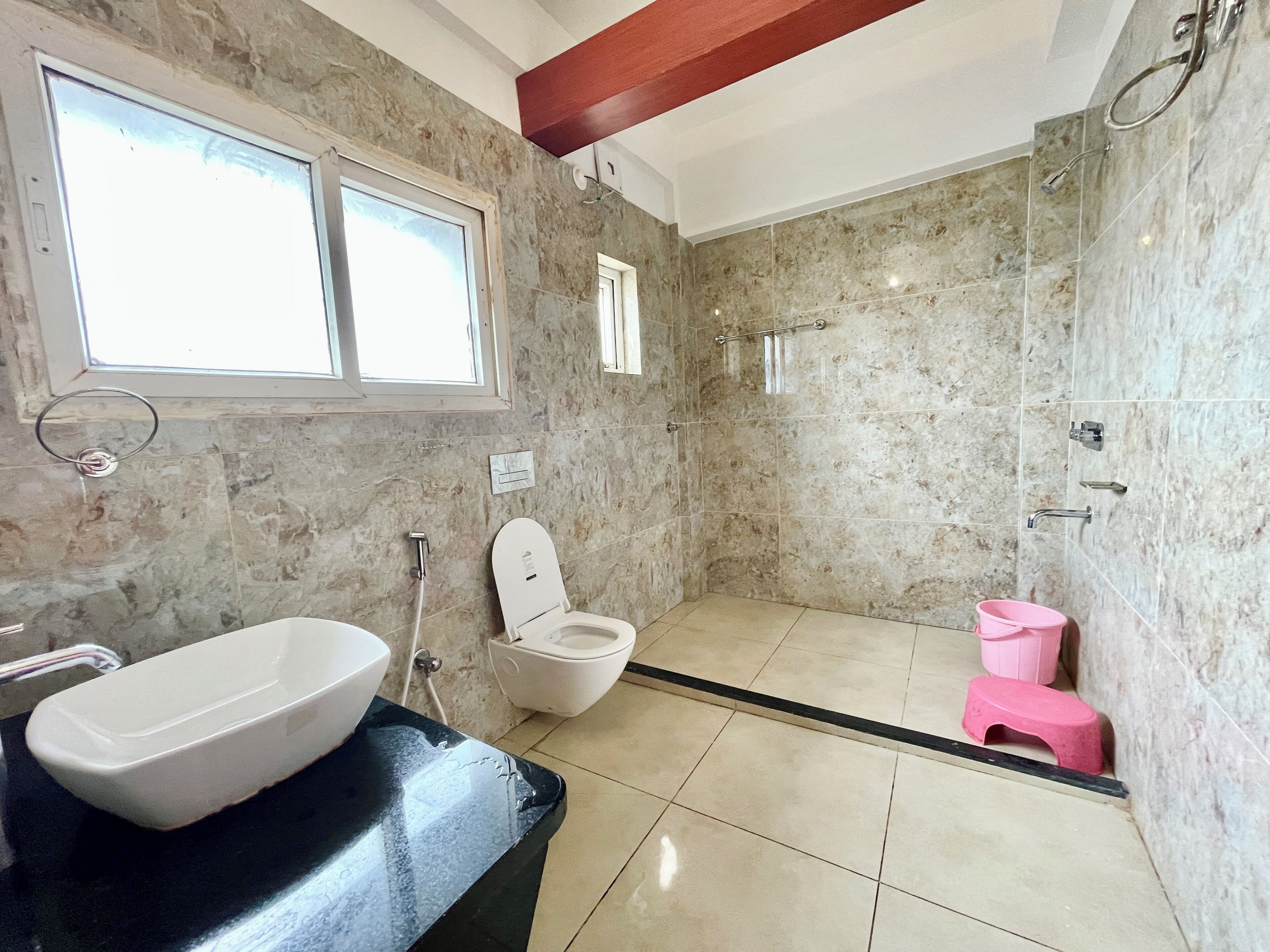 A bathroom with a large white sink, a toilet, a shower area, and a small pink stool.
