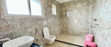 A bathroom with a large white sink, a toilet, a shower area, and a small pink stool.