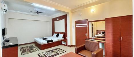 A hotel room with a bed, a desk, a chair, a table, a ceiling fan, and a wardrobe.