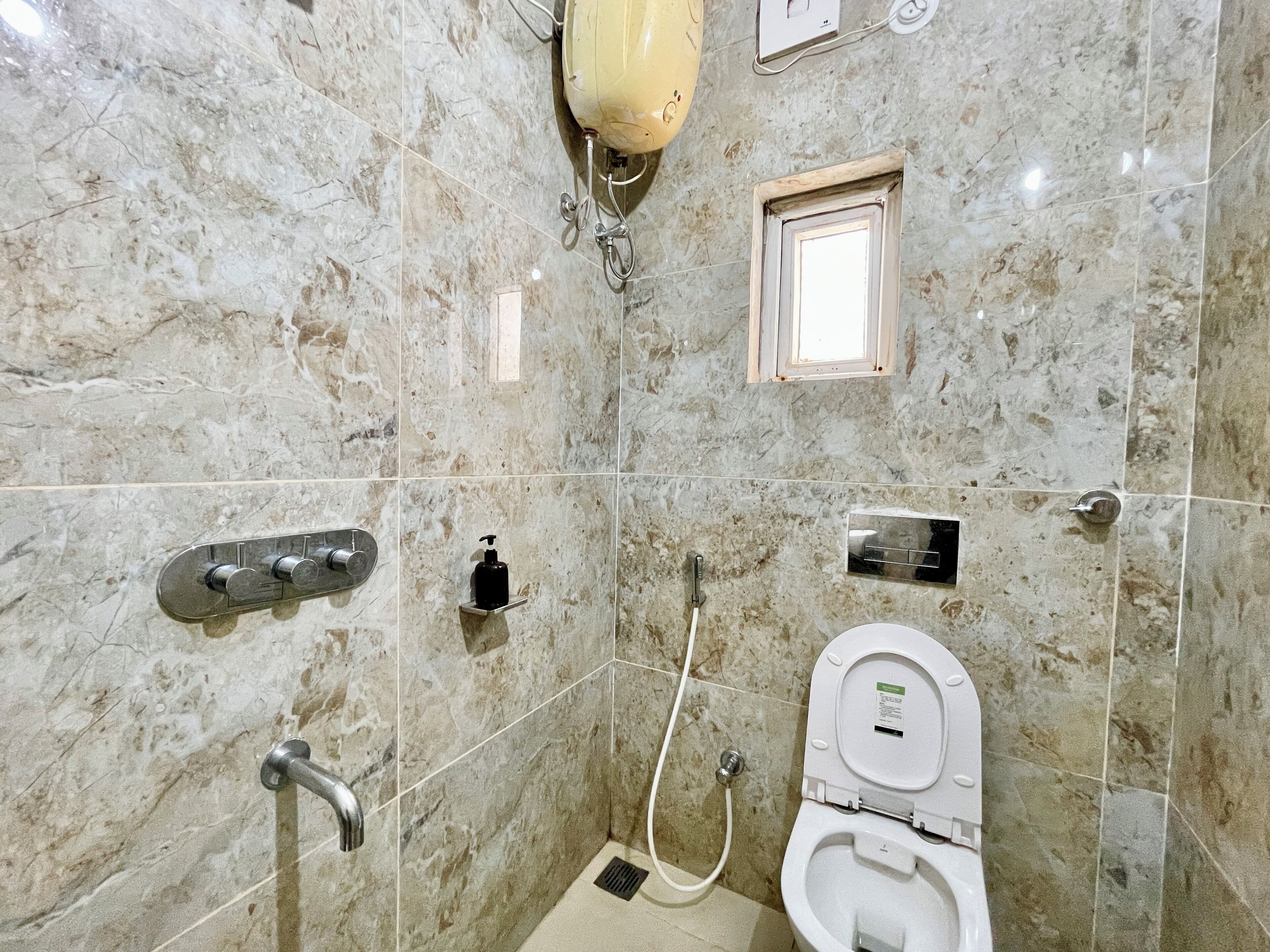 A bathroom with a marble floor, a white toilet, a shower with a handheld showerhead, and a soap dispenser.