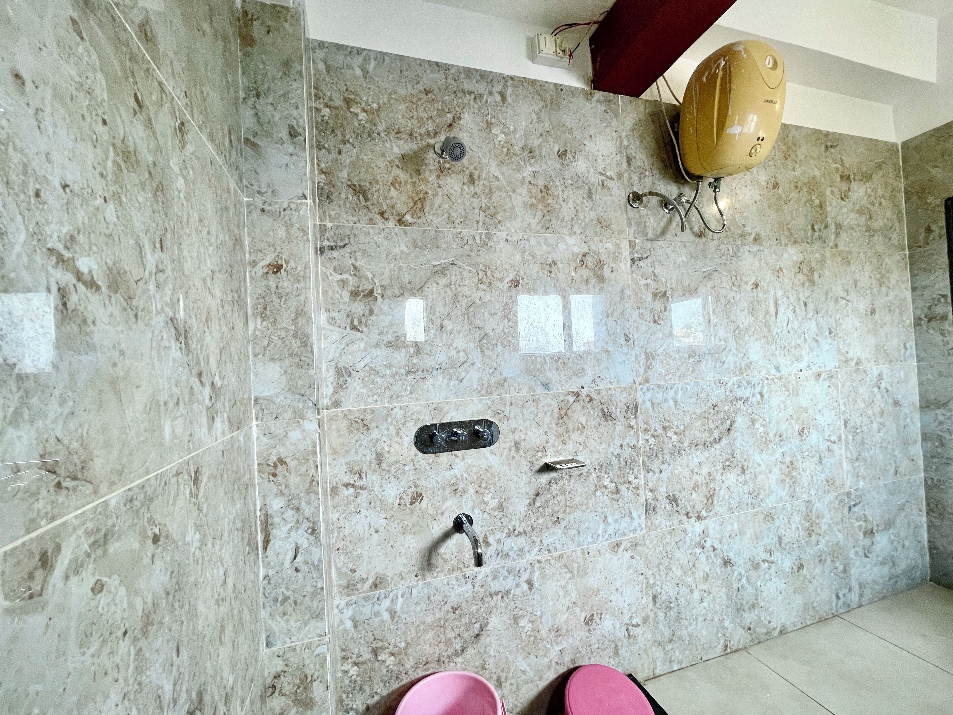 A bathroom with a marble wall, a showerhead, a towel rack, and a pair of slippers.