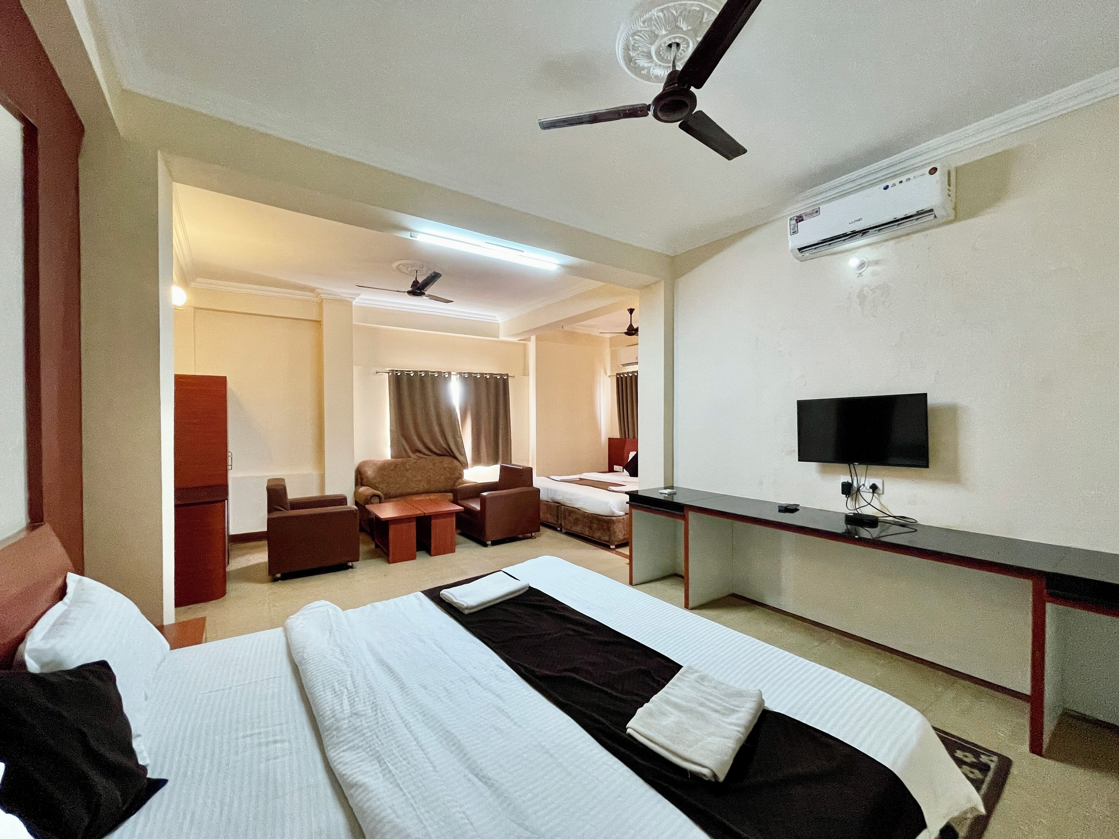 A hotel room with a bed, a desk, a chair, a television, and an air conditioning unit.