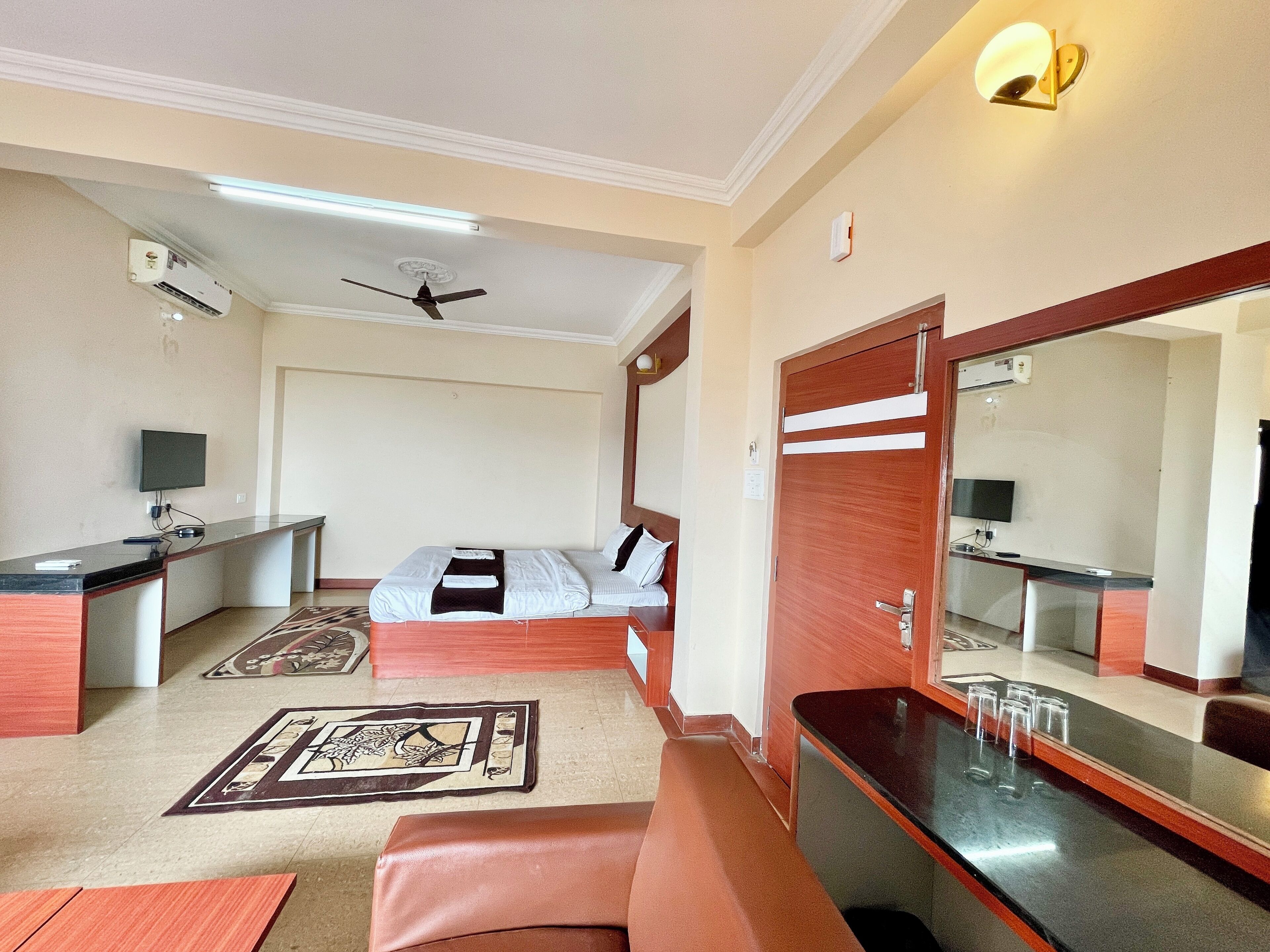 A hotel room with a bed, a desk, a mirror, a ceiling fan, and a television.