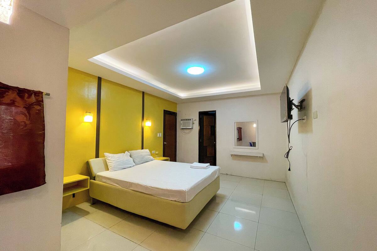 A modern hotel room with a large bed, a flat-screen TV mounted on the wall, and a ceiling light.