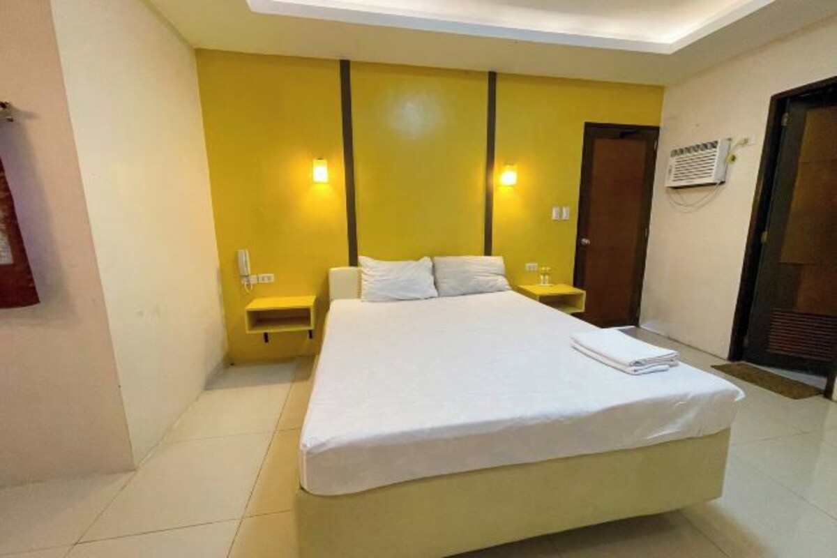 A hotel room with a large bed, two bedside tables, a wardrobe, and a ceiling light fixture.