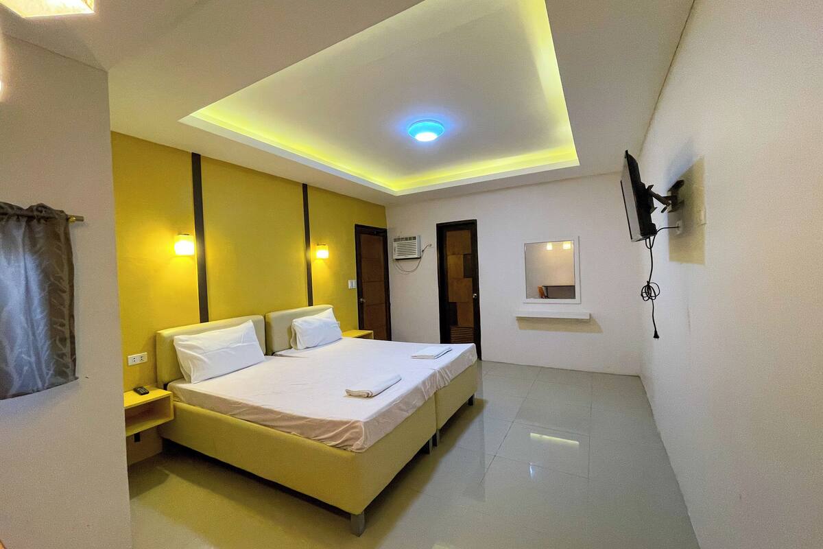 A hotel room with a bed, bedside table, nightstand, and a ceiling light.
