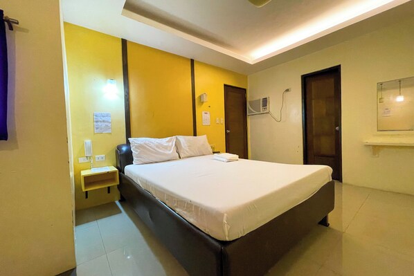 A hotel room with a bed, a nightstand, a wall-mounted air conditioner, and a door. - Casanova Inn (Bamban)