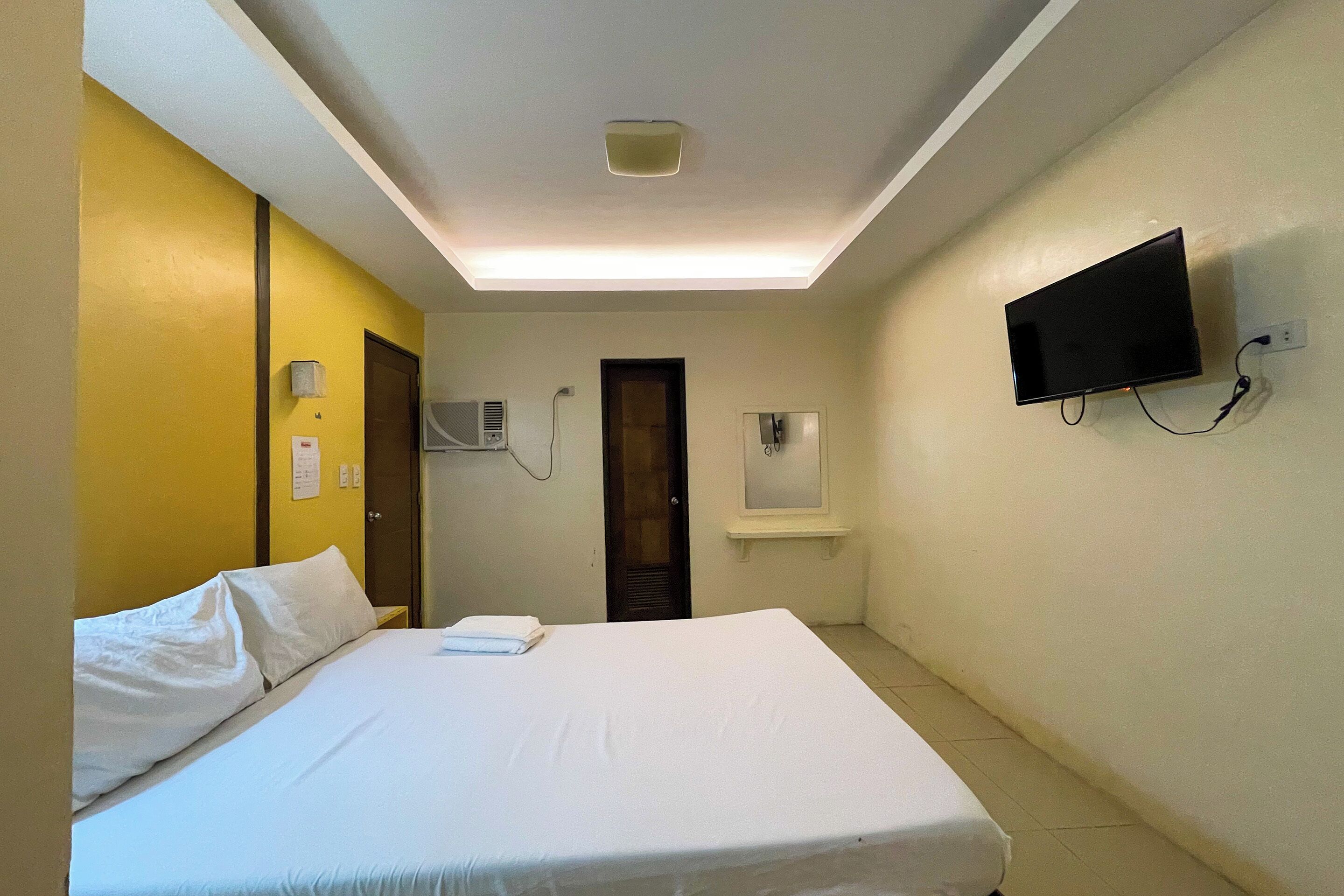 A hotel room with a bed, a television mounted on the wall, and a window with blinds.
