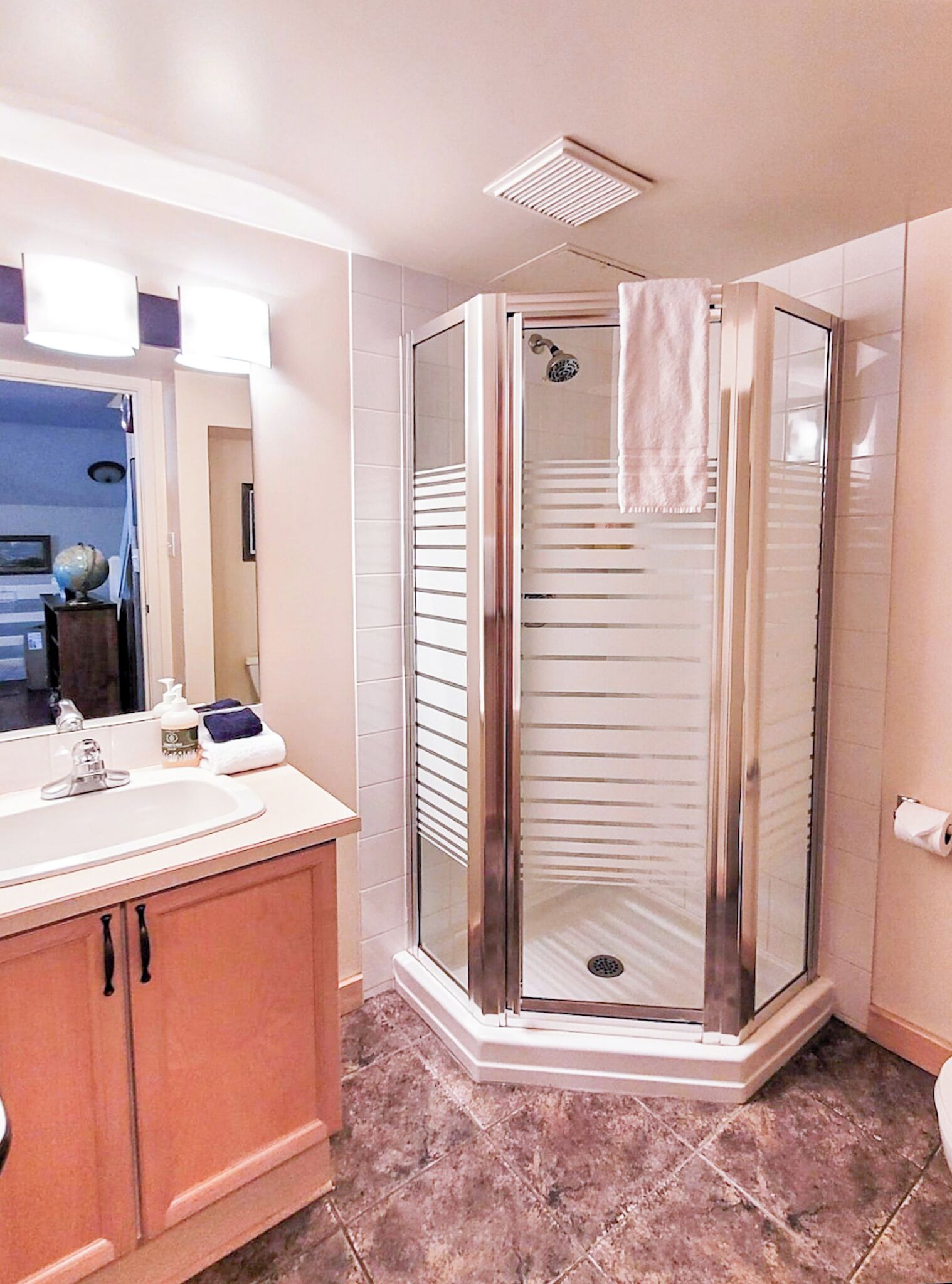 A modern bathroom with a glass-enclosed shower, a vanity with a sink and mirror, and a tiled floor.