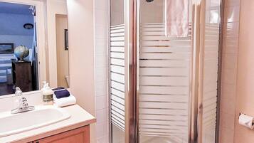 A modern bathroom with a glass-enclosed shower, a vanity with a sink and mirror, and a tiled floor.