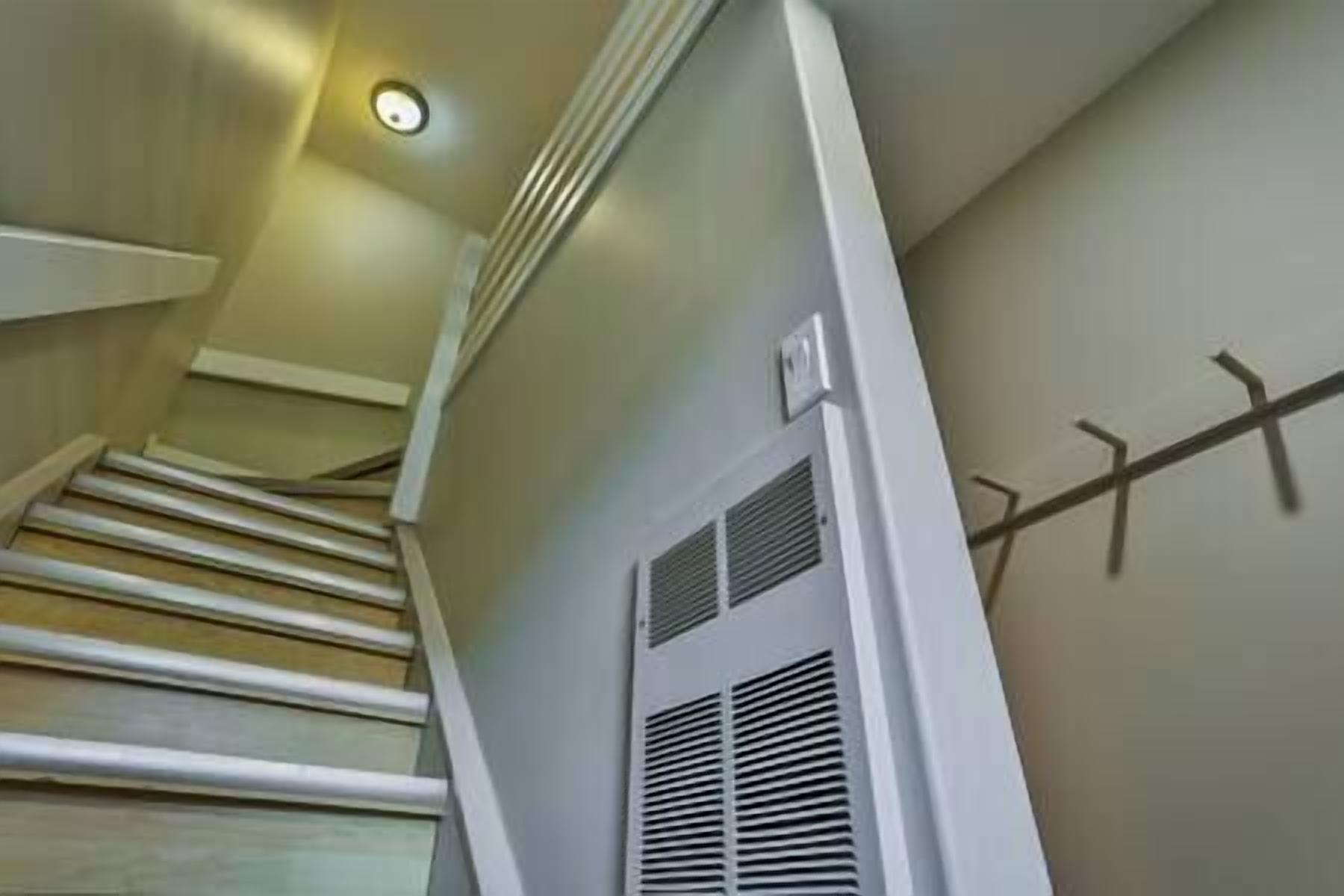 A staircase with a handrail, a wall-mounted vent, and a light fixture.