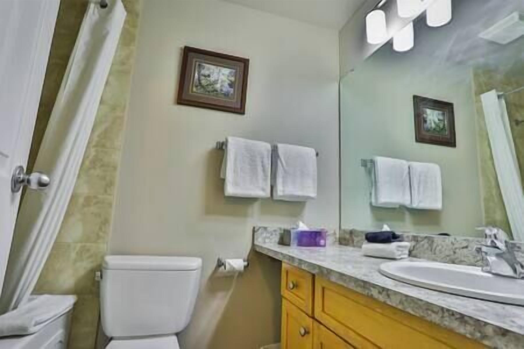 A bathroom with a toilet, a sink, a mirror, and towels hanging on the wall.