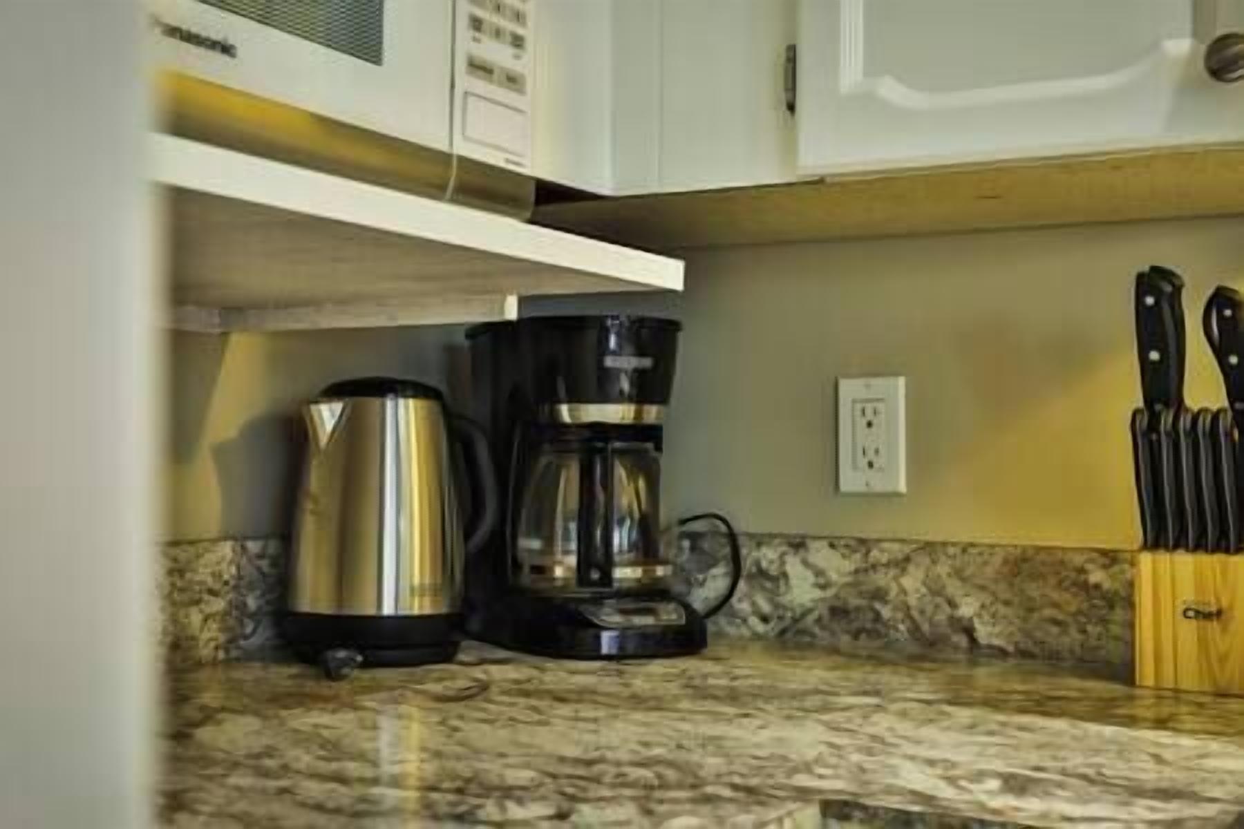 A kitchen with a coffee maker, a kettle, and a knife block on the counter.