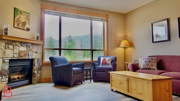 A cozy living room with a stone fireplace, two armchairs, a wooden coffee table, and a red sofa.