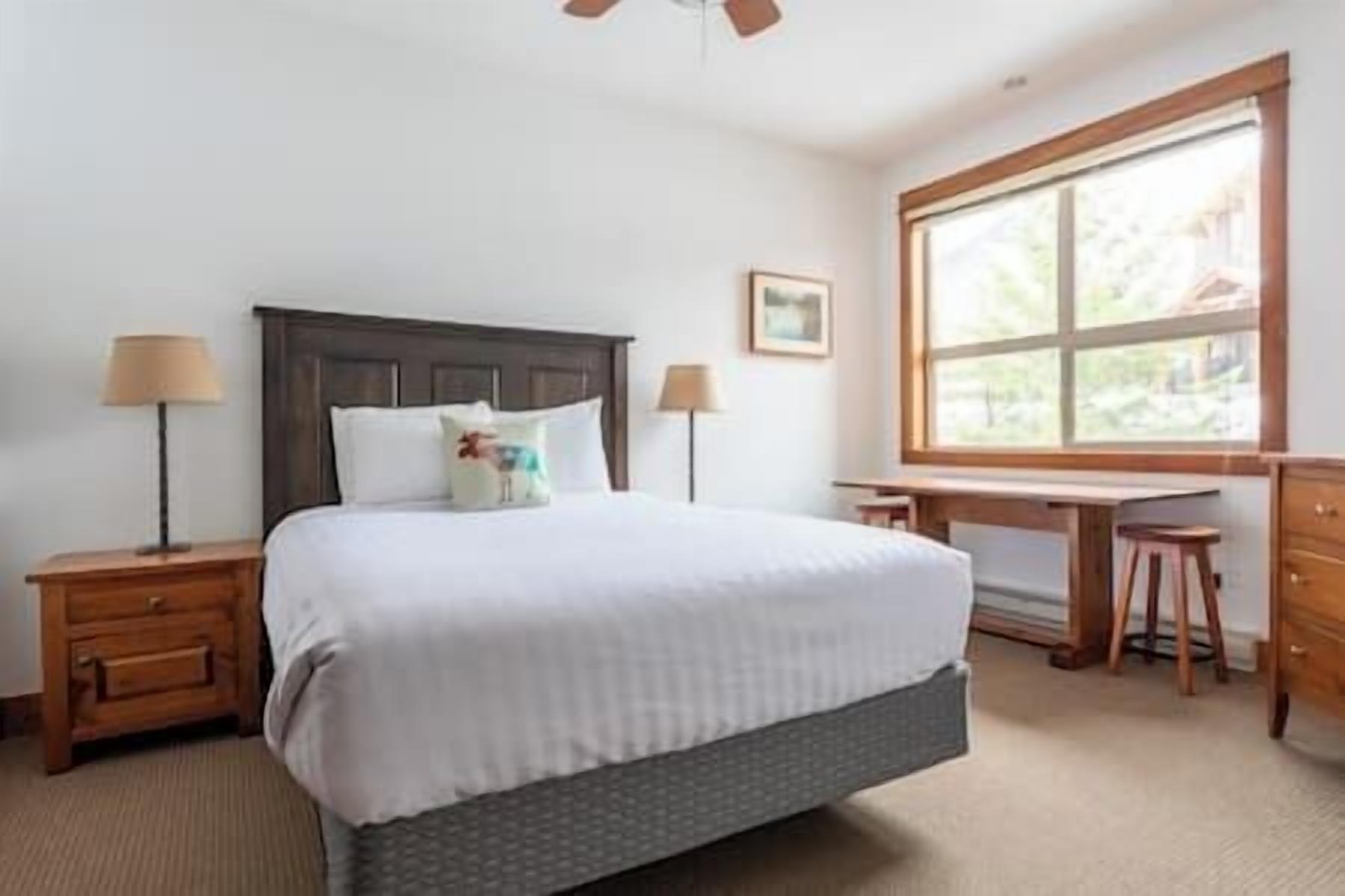 A neatly arranged bedroom with a bed, two bedside tables, a desk, and a window.