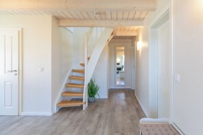 Un couloir avec un escalier en bois, une plante en pot et un banc.