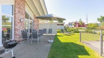 En terrasse med udendørs møbler, grill og et overdækket område med parasol.