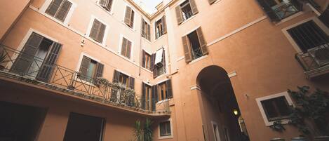 Une cour intérieure avec une arche centrale, des plantes en pot et un bâtiment doté de nombreuses fenêtres et de balcons.