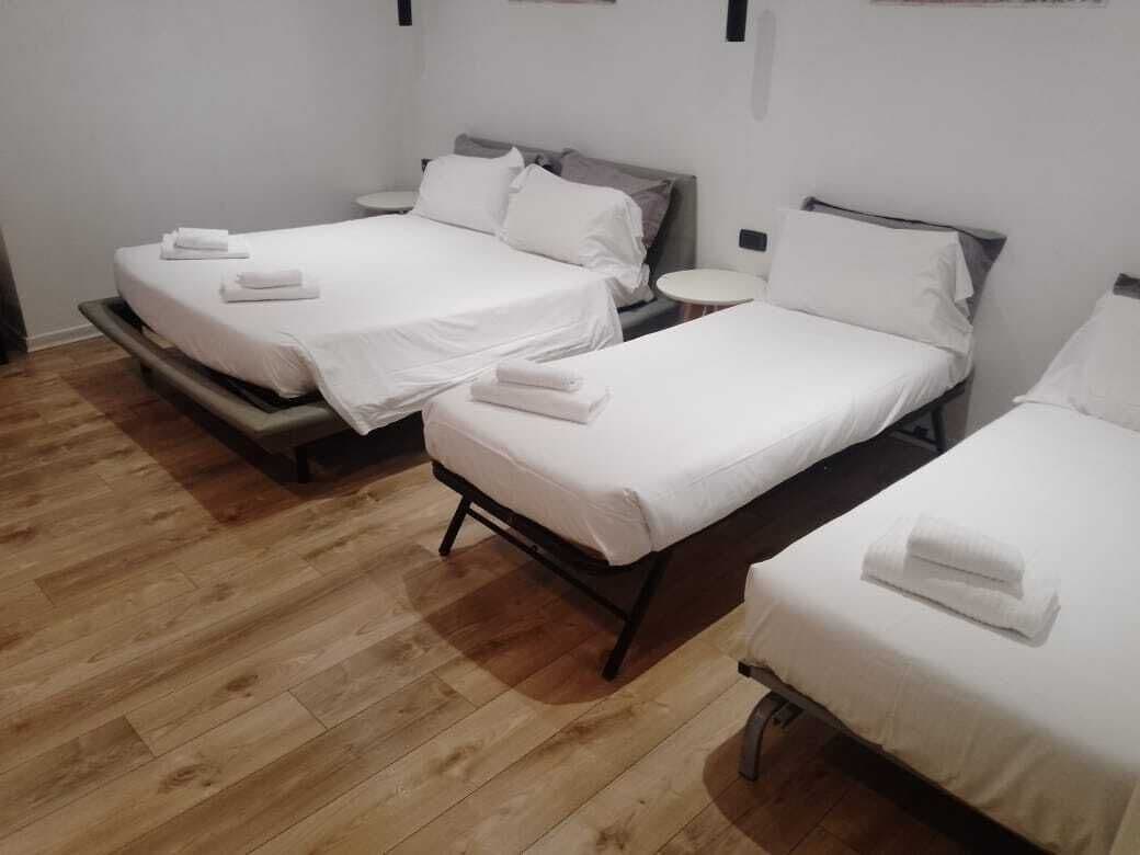 A hotel room with three beds, each with white linens and towels. The room has a wooden floor and white walls.