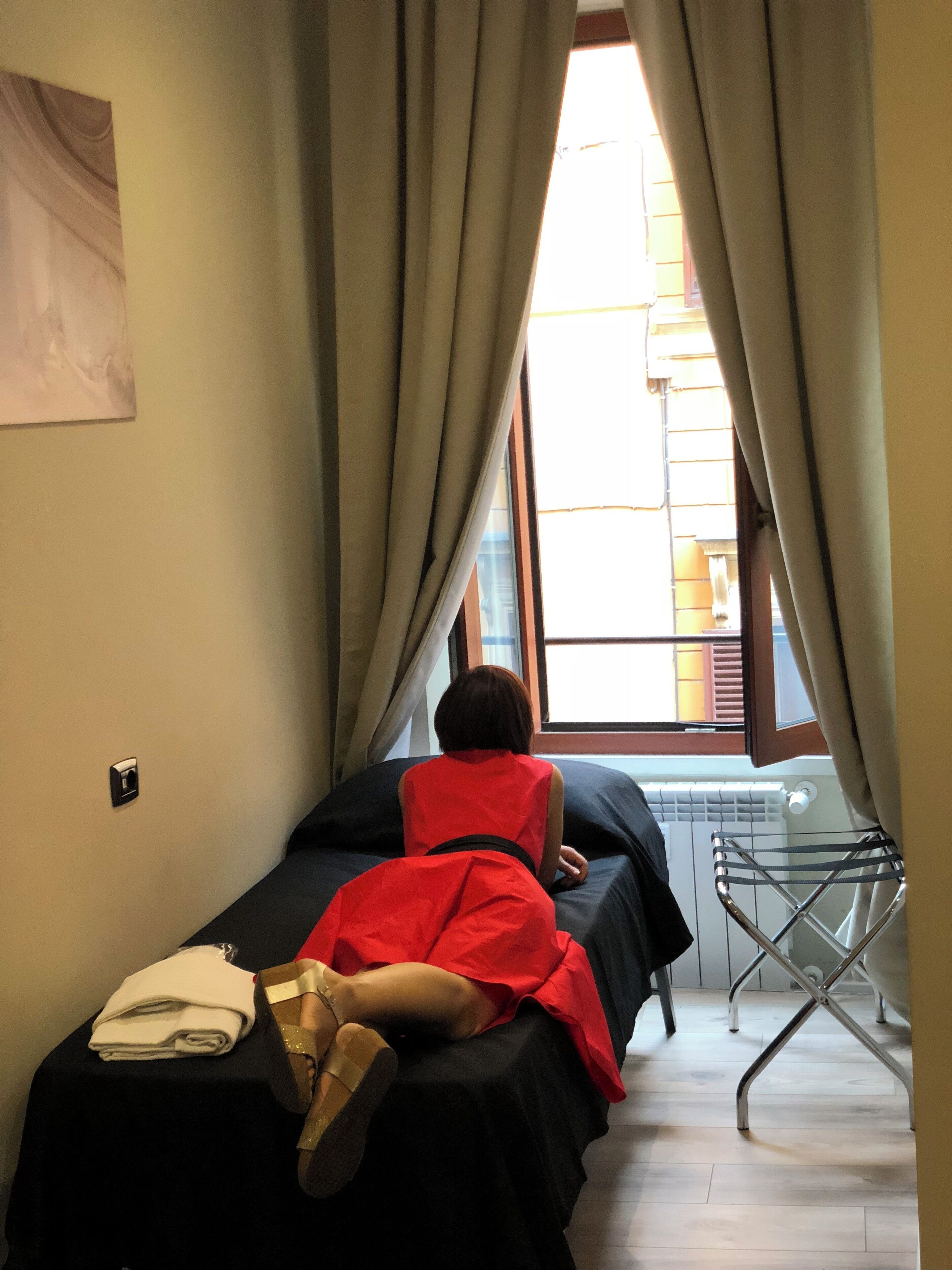 A narrow room with a bed, a radiator, and a window with curtains.