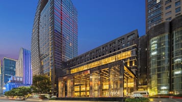 A modern hotel with a glass facade, large windows, and a prominent entrance with a decorative metal gate.