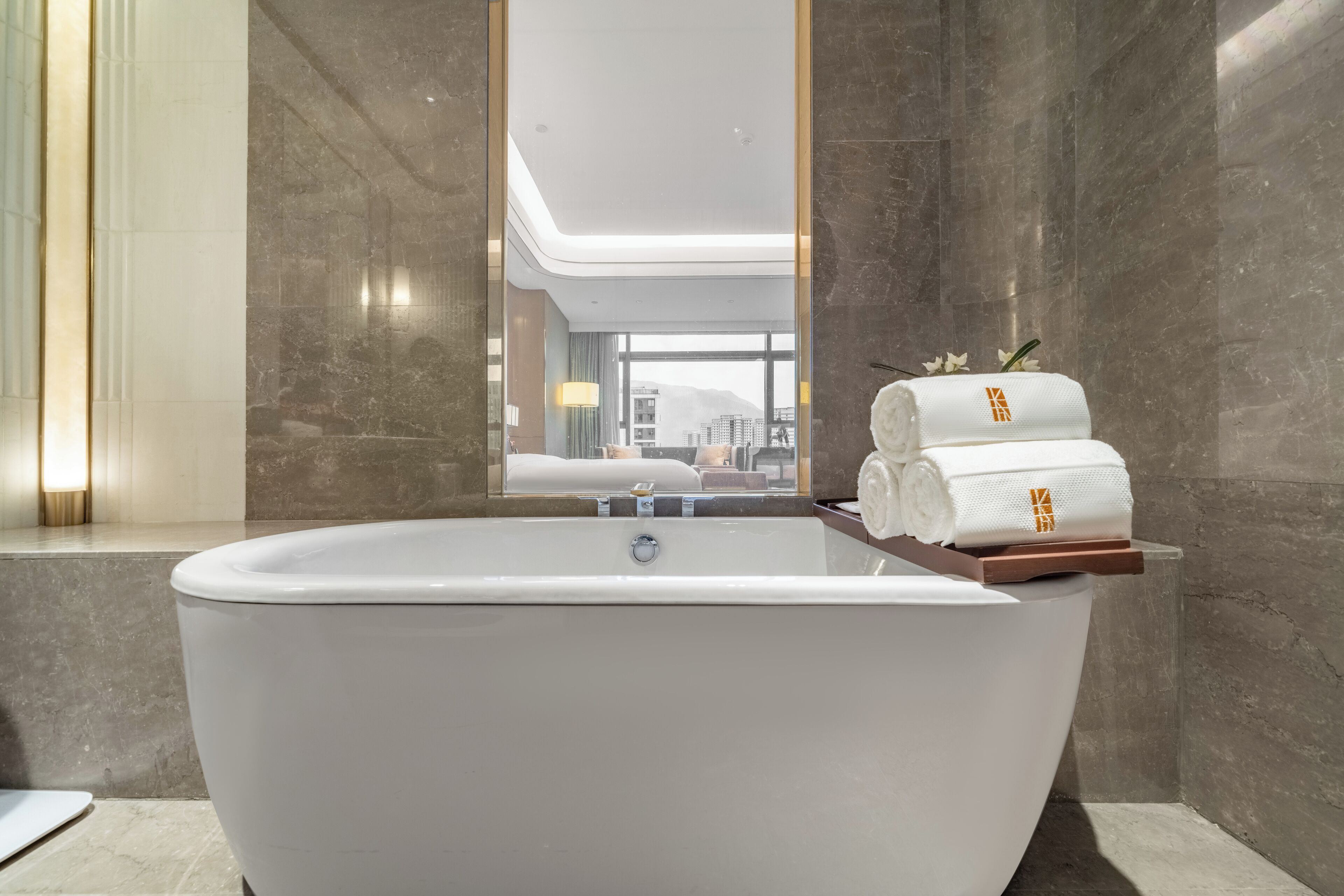 Ein modernes Badezimmer mit einer freistehenden Badewanne, einem großen Spiegel und Blick auf die Stadtlandschaft durch das Fenster.
