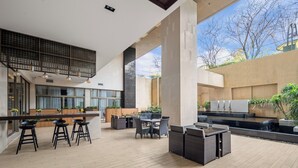 Un espace de restauration extérieur moderne, doté de hauts plafonds, de grandes fenêtres et offrant une vue sur les arbres.